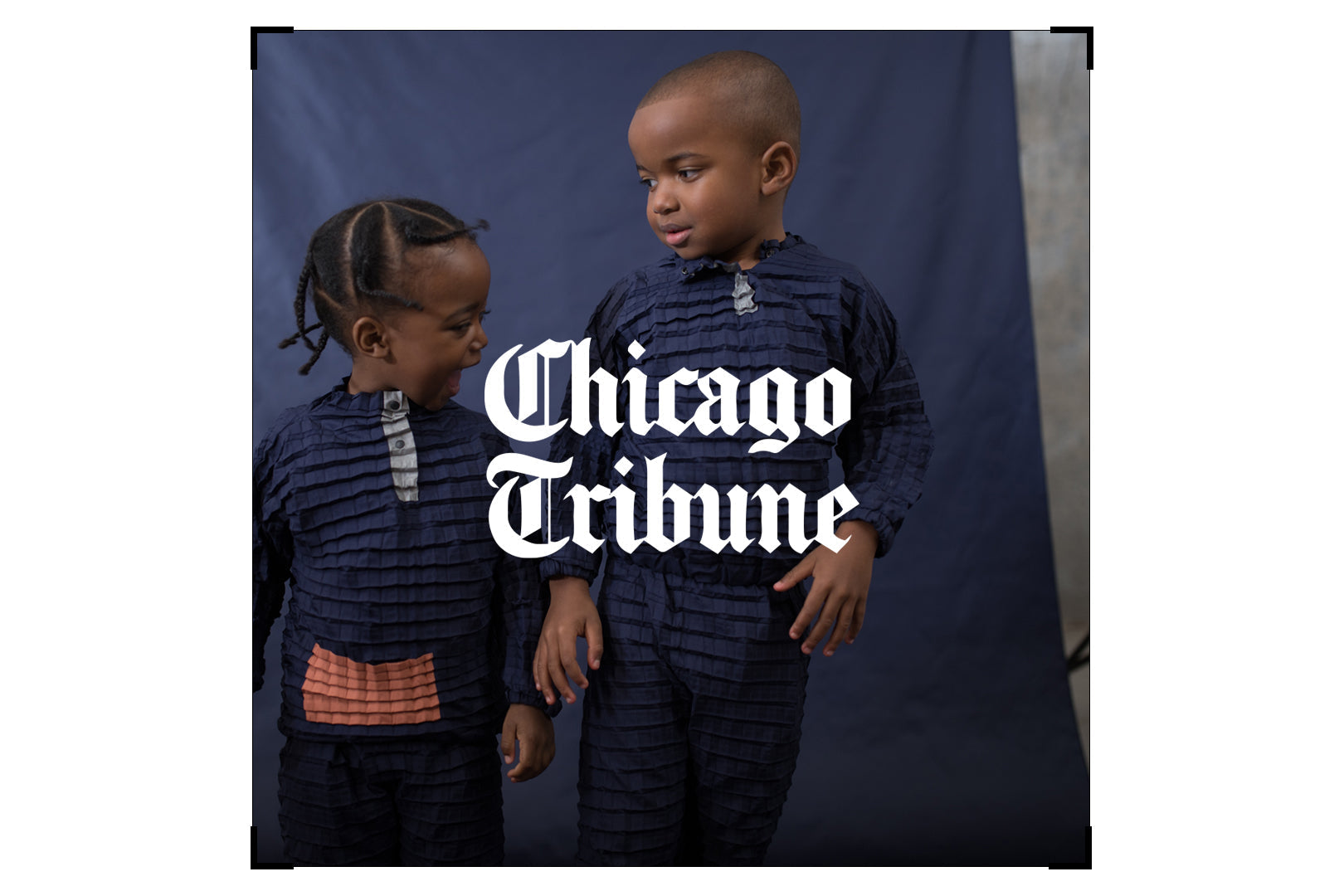Two children in matching Orion Blue Petit Pli outfits stand together, featured in the Chicago Tribune’s story on ethical kidswear.