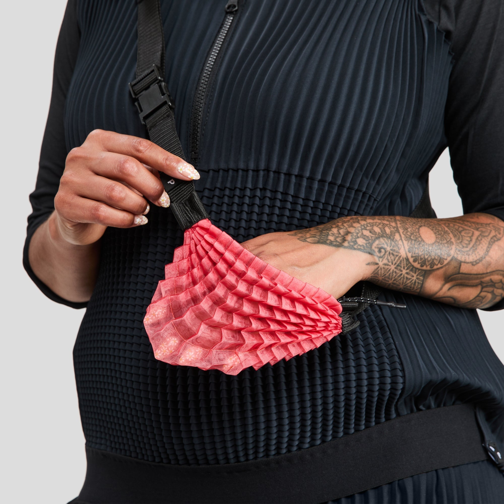 Model in dark outfit modelling small red accordion‑textured accessory - Petit Pli's SAT.PAK