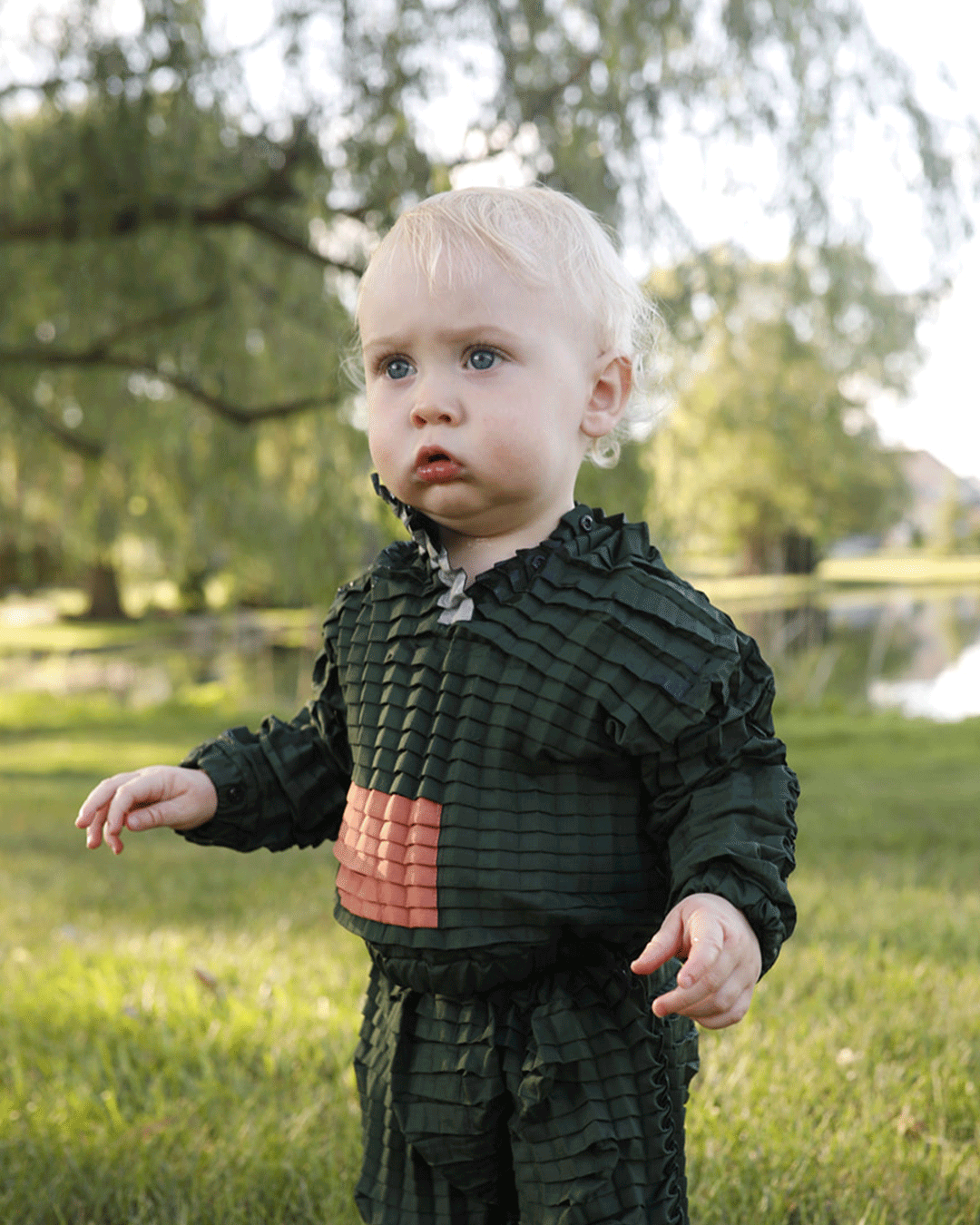 Emma son wearing Petit Pli Green Ore Suit stood in a wonderfully green park