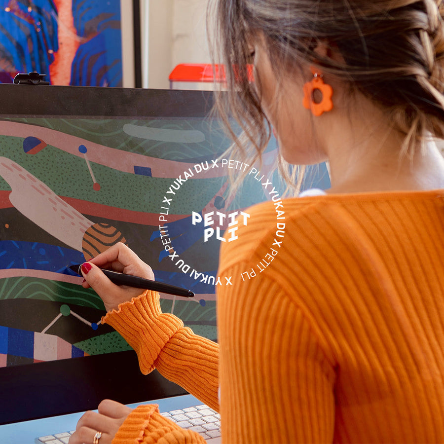 Yukai Du in an orange sweater uses a stylus on a tablet, creating a colourful abstract world for Petit Pli’s Print 09.