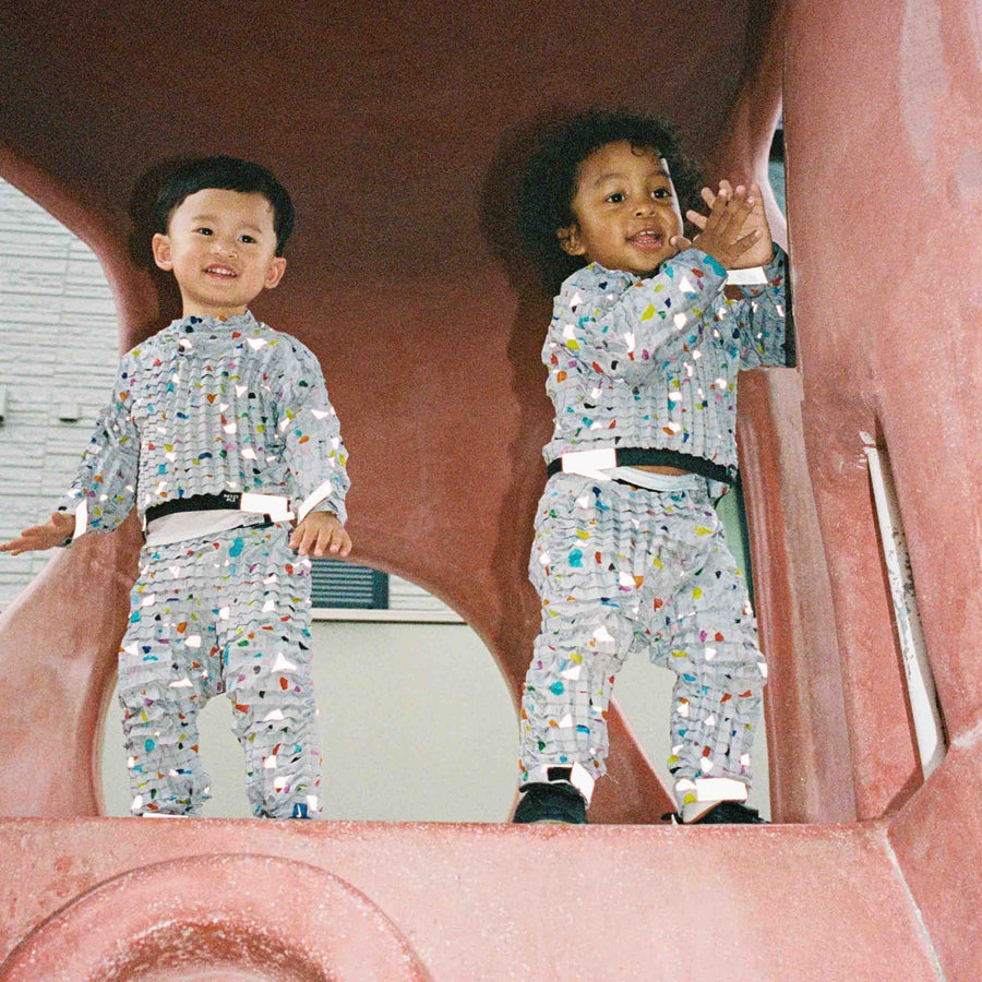 Two children in Petit Pli’s Memphis-inspired outfits play inside Japan’s red octopus playground, blending bold design with joyful exploration.