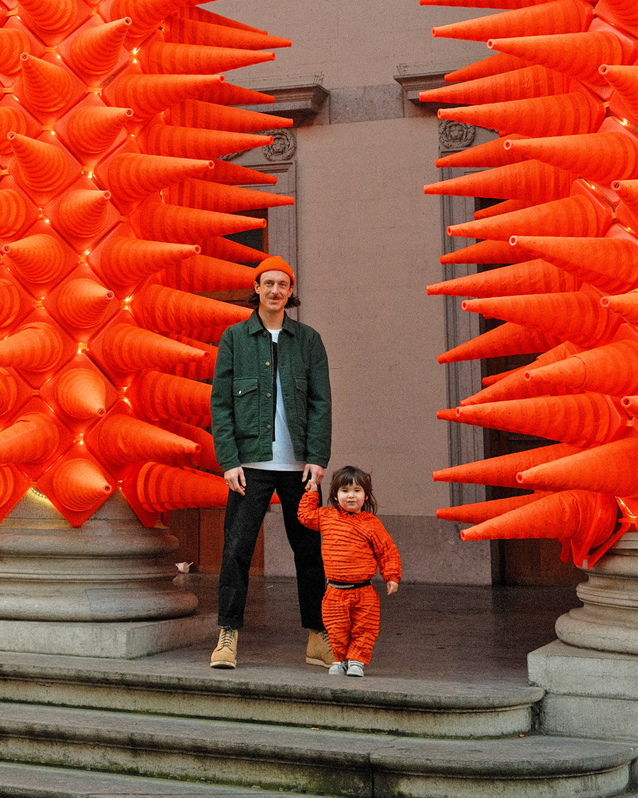 Father and son stand before a grand building and bright orange cone art, capturing playful moments and Petit Pli’s spirit of turning memories into keepsakes.