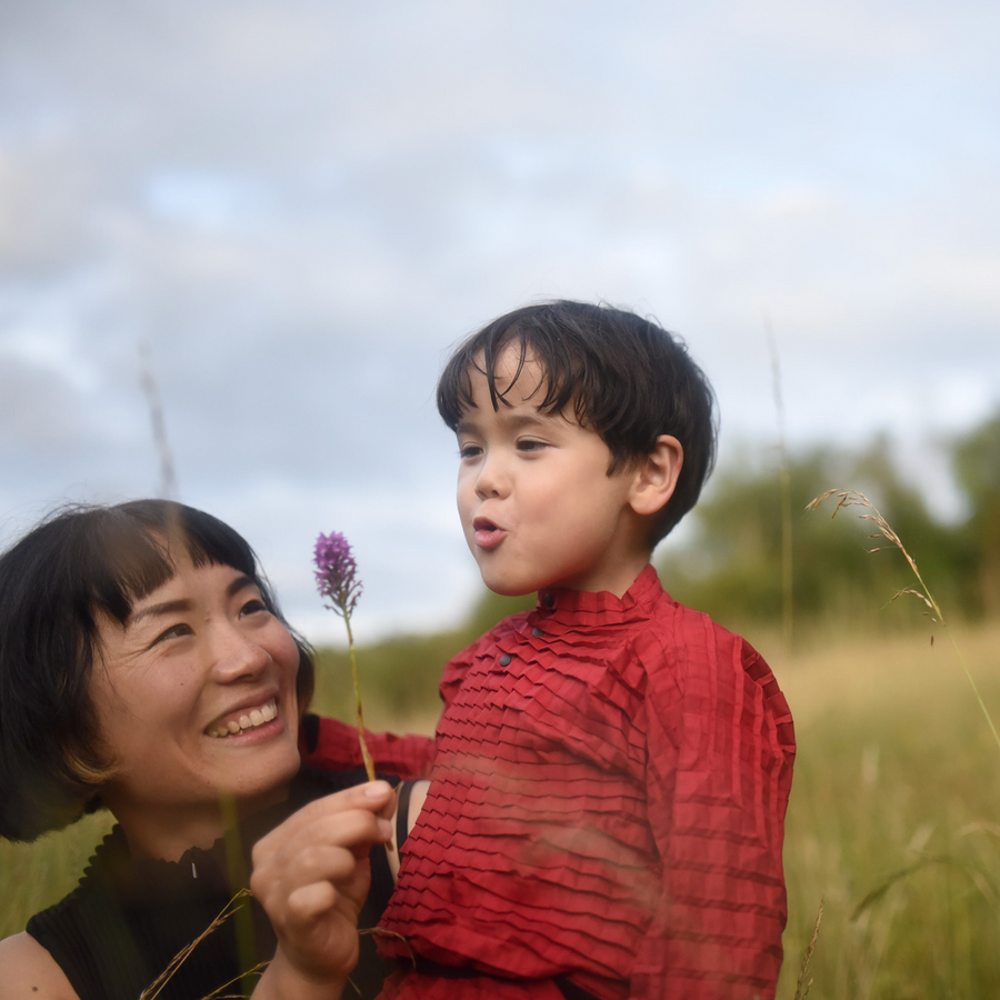 Adult and child share a joyful moment in a grassy field, holding a flower and exploring nature together, capturing the spirit of summer adventure in London.
