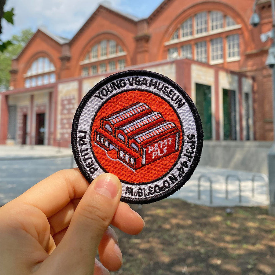 Young V&A embroidered patch in front of the museum’s red‑brick building in Bethnal Green, celebrating the Young V&A identity and creative spirit.