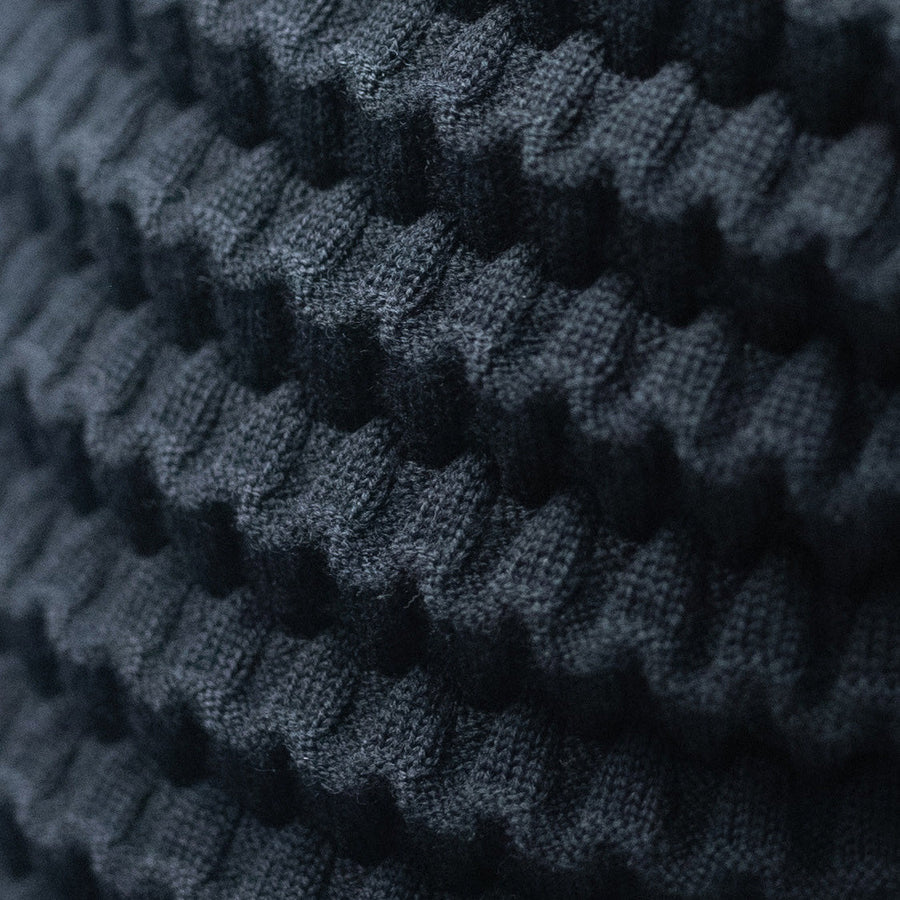 Soft, dark merino wool fabric with raised, tile‑like knit pattern, showcasing Petit Pli’s Knot‑Tile® innovative expandable design.