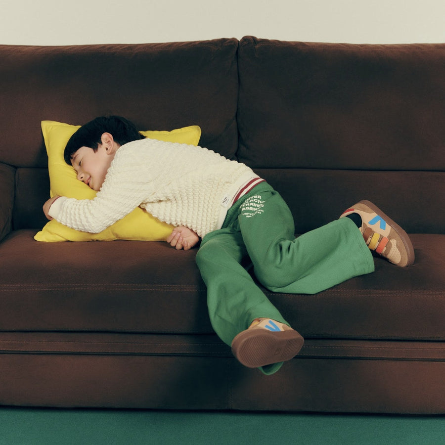 A LittleHuman asleep on a yellow cushion in a Milky Way Merino Jumper, from the VEJA campaign shoot