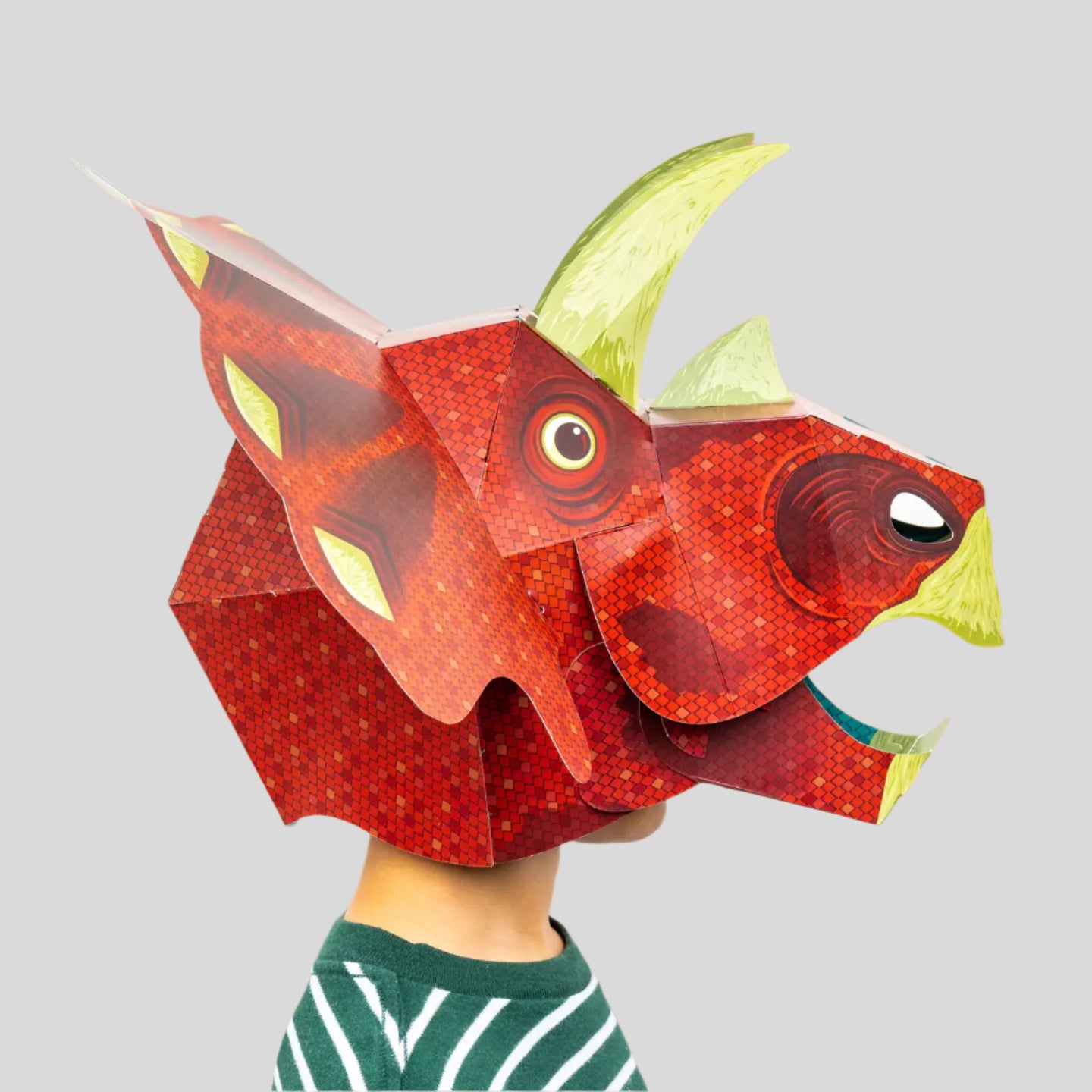 Red dinosaur mask with green horns on a person against a grey background